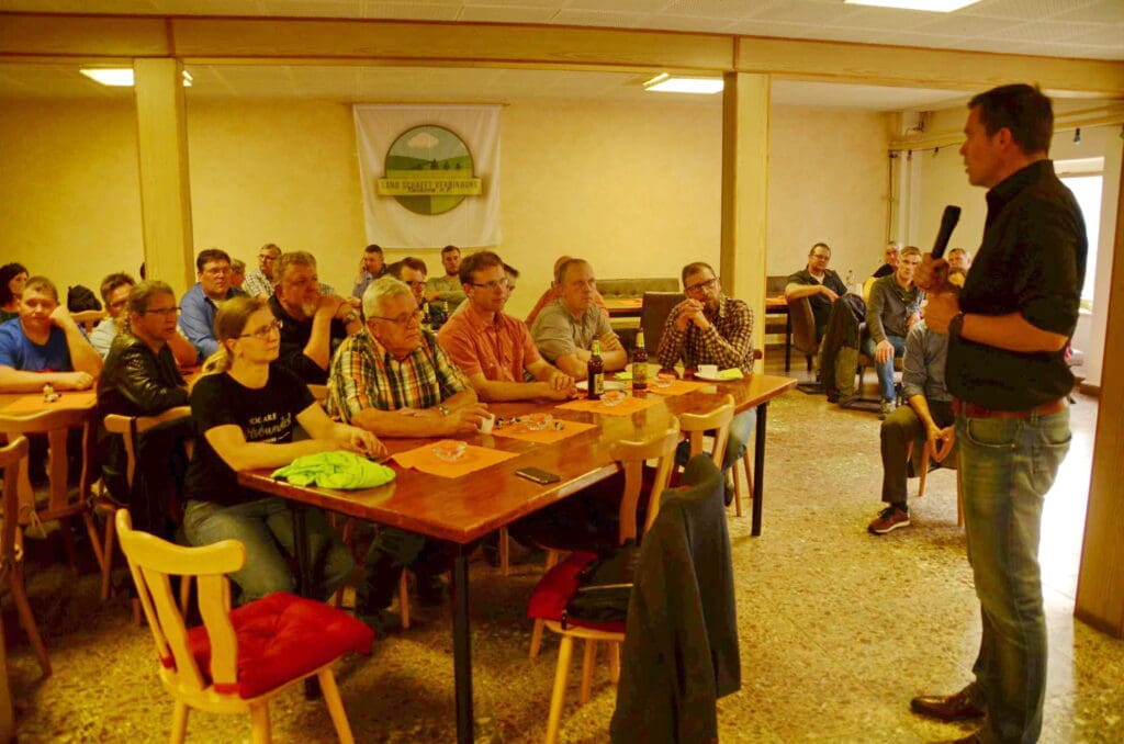 Der FDP-Abgeordnete Gero Hocker steht rechts im Bild vor einer Gruppe sitzender Landwirte. Im Hintergrund ist das sächsische LsV-Logo an der Wand befestigt.