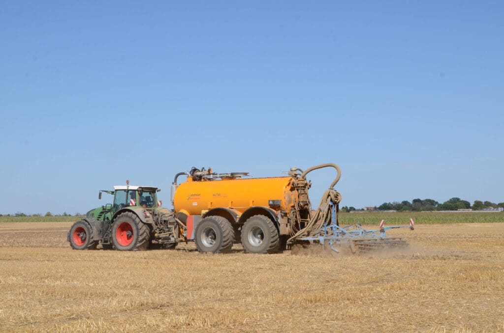 Ein Traktor zieht ein Güllefass über einen abgeernteten Getreideacker.