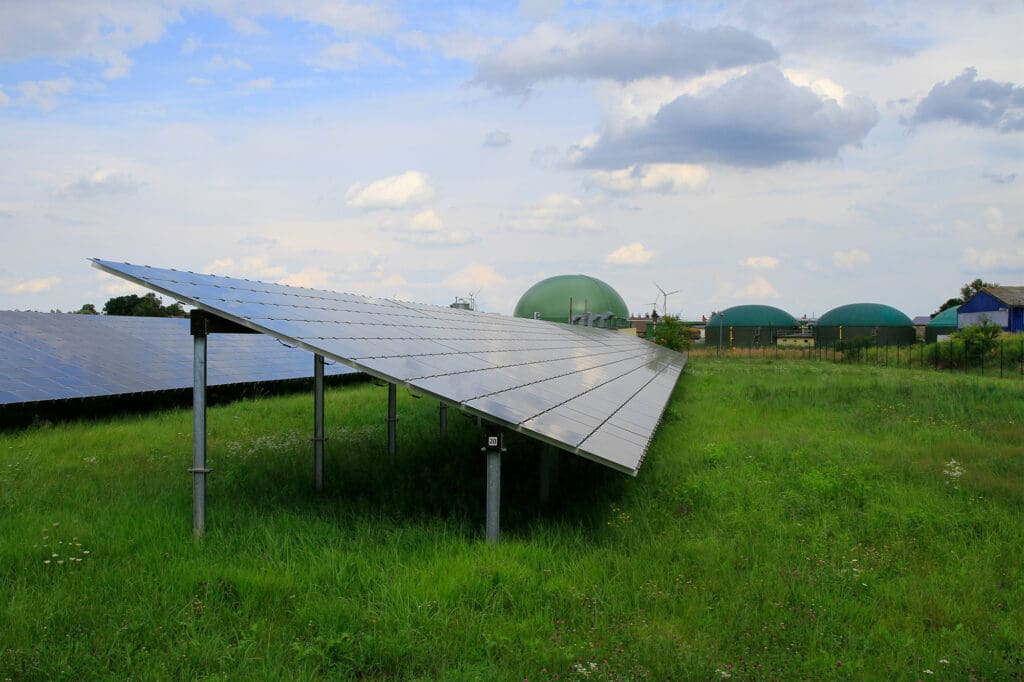 Solarmodule (Photovoltaik) auf Grünland, daneben steht eine Biogasanlage