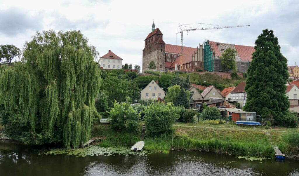 Der Havelberg mit der Havel im Vordergrund und mehreren Häusern am Hang.